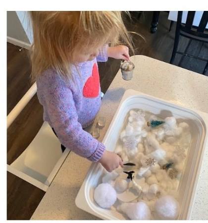 Toddler scooping cotton balls from a winter-themed sensory bin