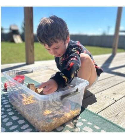 Little boy exploring a sensory bin outdoors and naming what he finds